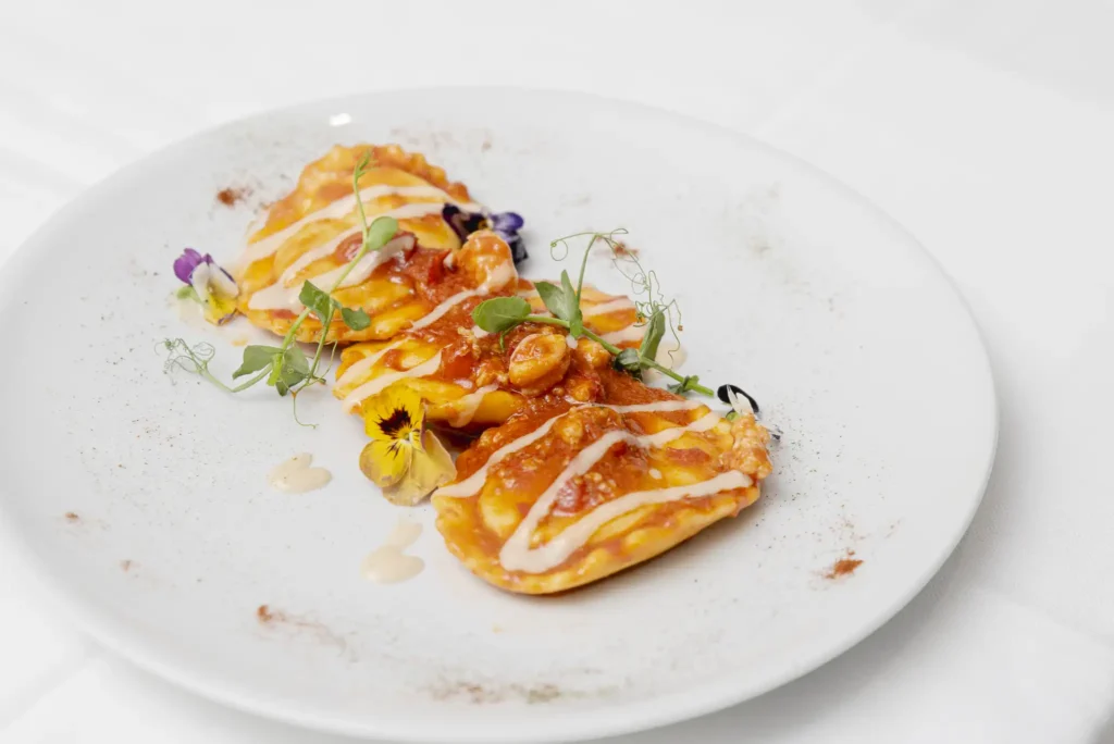 “Ravioli gourmet con salsa al pomodoro e crema leggera, decorati con fiori eduli – Rama Eventi”